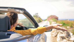 Woman driving a convertible with her arm out the window symbolizing travel by car and business trips