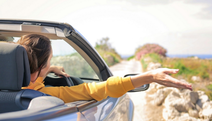Woman driving a convertible with her arm out the window symbolizing travel by car and business trips